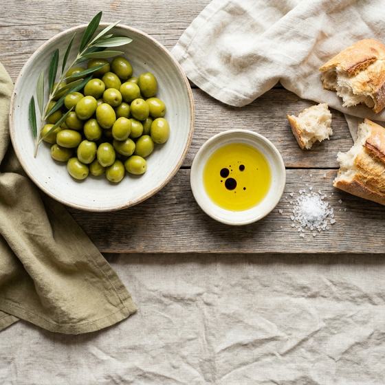 Μπολ με πράσινες ελιές Χαλκιδικής, ελαιόλαδο και ψωμί σε ξύλινο τραπέζι